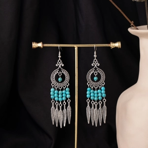 Detail of bohemian silver earrings with blue beads and metal feather pendants on a stand