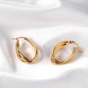 Detail shot of golden triple-layered interwoven hoop earrings on white satin fabric