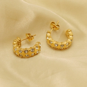 Macro detail of gold C-shaped earrings with rhinestones on champagne silk background
