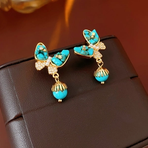 Détail de boucles d'oreilles papillon dorées avec pierres turquoise sur un écrin