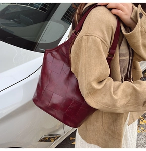 Detail van bordeauxrode leren shopper met geometrische stiksels op de schouder van een model