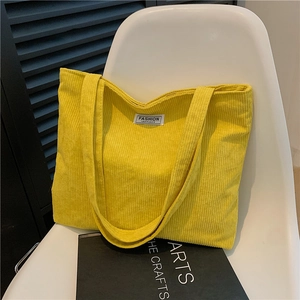 Stylish yellow corduroy tote bag with wide strap on a white chair in a home setting