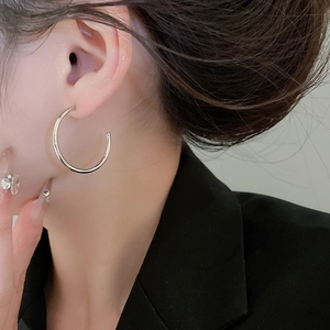Detailed close-up of a large polished silver C-shaped hoop earring on a model