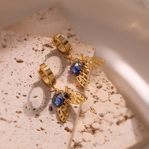 Gold bee earrings with blue gems and openwork design on a textured stone base