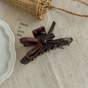 Close-up of elegant burgundy acetate bow hair claw clip on a rustic fabric background