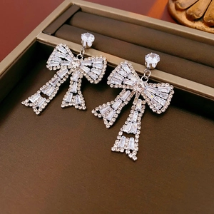 Detailed macro view of silver bow-shaped earrings featuring sparkling rhinestones in a box