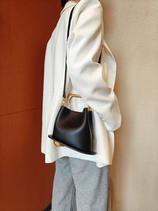 Detail of the unique gold metal handle and black leather texture of the bucket bag
