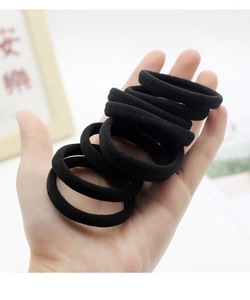 Detail showing high-elasticity seamless black hair ties held in hand for size comparison
