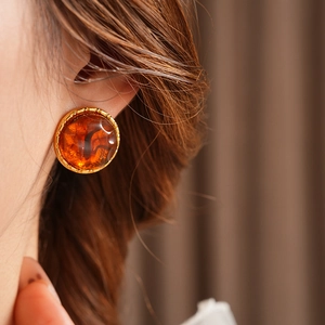 Close-up of amber resin round stud earrings with golden textured metal on a model's ear