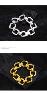Close-up of chunky gold and silver hollow link bracelets on a textured black stone surface