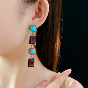 Model wearing vintage gold drop earrings with blue round and burgundy square gemstones