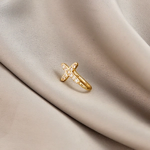 Detail of gold cross ear cuff with micro-paved zircons on elegant beige silk fabric