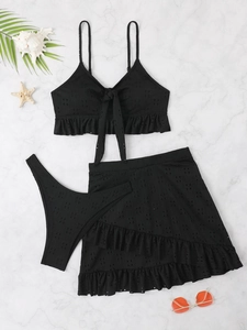 Flat lay detail of black hollow-out three-piece bikini set with ruffles on marble backdrop