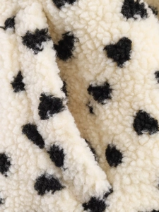 Close-up of soft beige sherpa fleece fabric featuring minimalist black heart patterns
