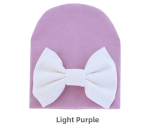 Detail of light purple baby knit hat featuring a large white bow on soft cotton fabric