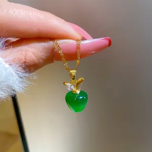 Macro shot of an apple pendant necklace with green cat-eye stone on a golden chain