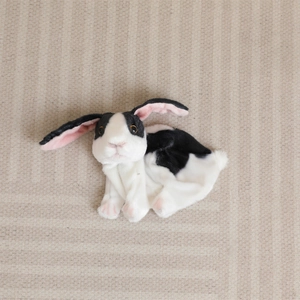 Gros plan d'un lapin en peluche noir et blanc aux oreilles roses sur un tapis rayé