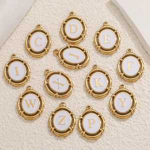 Detailed shot of oval gold A-Z initial pendants with white enamel on textured background