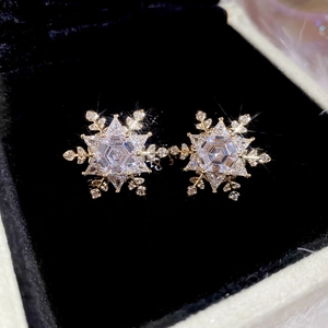 Macro shot of gold snowflake stud earrings with sparkling crystals on black velvet