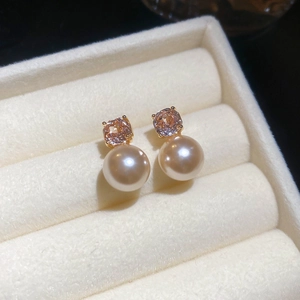 Macro shot of gold-plated pearl earrings with pink zircon on a beige velvet jewelry box