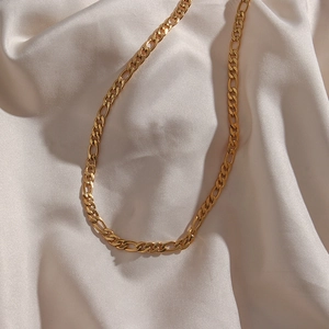 Close-up of a 5mm golden Figaro chain necklace on a soft white silk background