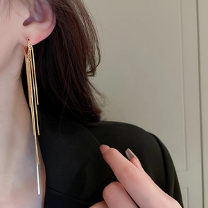 Close-up of elegant gold plated teardrop tassel earrings worn by a model in black