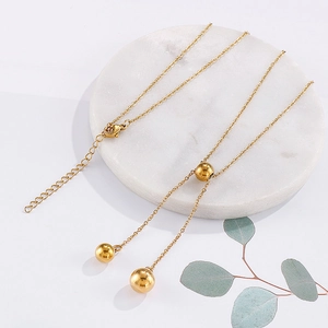 Minimalist gold stainless steel ball bead necklace on white marble with eucalyptus accent