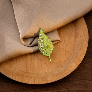 Detailed view of a green leaf brooch with white pearls on a rustic wooden tray