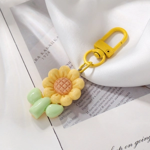 Detailed close-up of a handmade yellow sunflower keychain on soft silk and newsprint