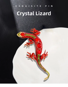 Detailed close-up of crystal lizard brooch with red and green stones on gold base
