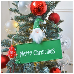 Detail of green metal Merry Christmas sign with plush Santa decor hanging on tree