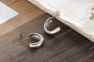 Close-up of polished silver C-shaped chunky hoop earrings on a rustic wooden background