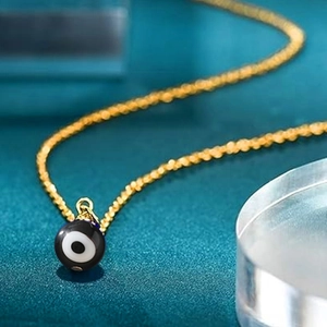 Detail of a gold snake chain necklace with a black round evil eye protection charm