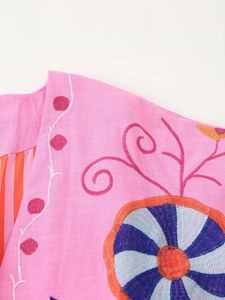 Close-up detail of colorful ethnic embroidery and linen fabric texture on pink cardigan