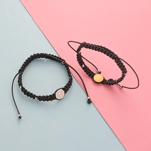 Close-up of Saint Benedict medal charms on black woven cords over pink and blue background