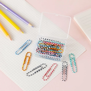 Flat lay of colorful striped paper clips in a clear box on a pink desk with grid paper