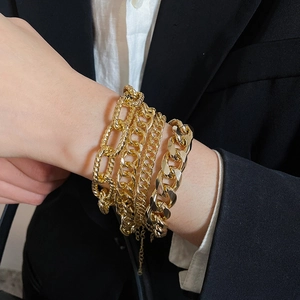 Close-up of layered chunky gold chain bracelets with various links on model's wrist