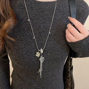 Dettaglio di collana lunga argentata con nappa, cuore di cristallo e cubo marmorizzato