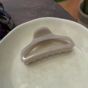 Close-up of a 10cm marbled light brown hair claw clip on a decorative beige tray