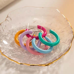 Colorful C-shaped enamel hoop earrings in stainless steel displayed on a glass tray