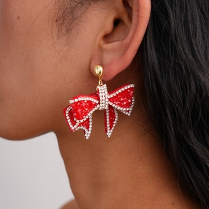 Close-up of model wearing large red rhinestone bow tassel earrings with gold studs