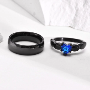 Macro shot of black titanium steel rings with a blue heart zircon on white stone surface