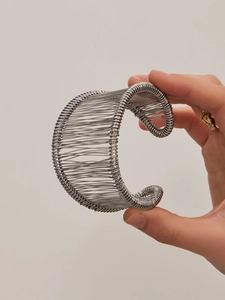 Gros plan d'un large bracelet manchette ouvert en fils d'argent sur un poignet