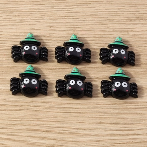 Flat lay of six glossy black cartoon spider charms with green hats for DIY crafts