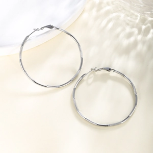Macro shot of silver-tone hoop earrings with precise textured chain pattern engraving