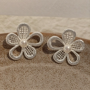 Hollow flower silver earrings with pearl inlay on a natural textured ceramic tray