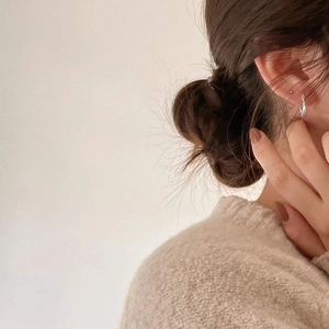 Close-up of minimalist silver twisted hoop earrings worn with a beige knitted sweater