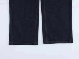 Gros plan sur l'ourlet du pantalon en jean bleu foncé avec surpiqûres jaunes contrastées