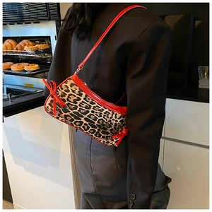 Close-up of leopard print baguette bag with red strap and bow in a cafe setting