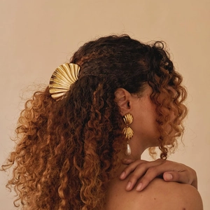Detail of a gold wavy shell hair claw and pearl drop earrings on a woman with curly hair
